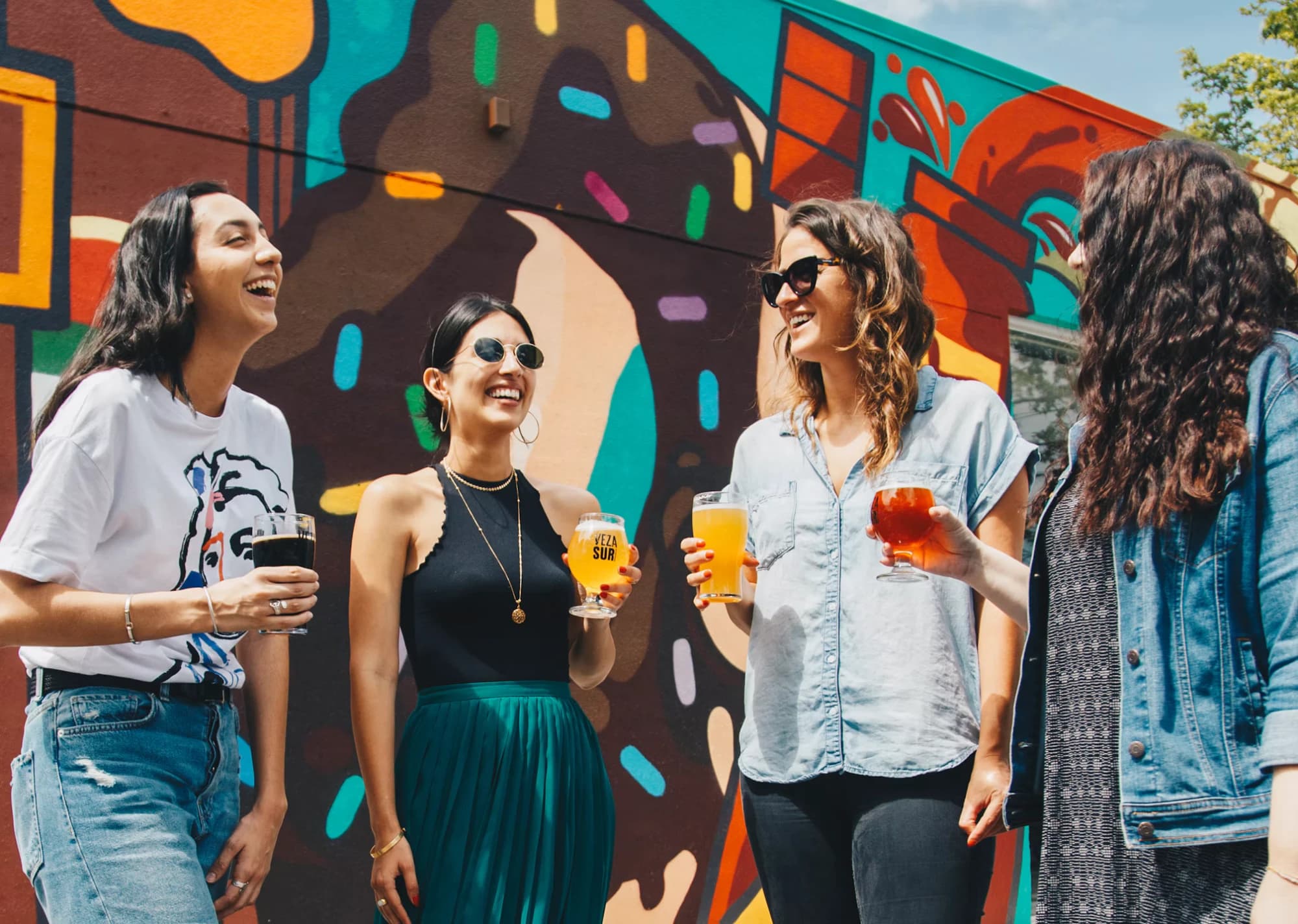 Friends laughing with drinks in front of a colourful mural